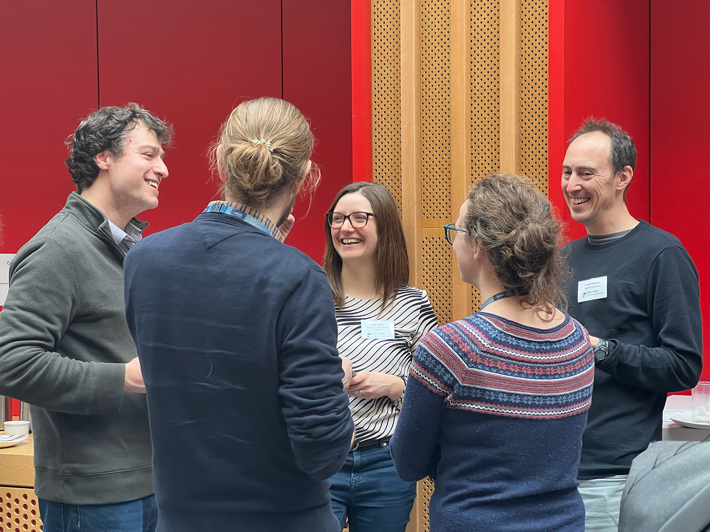 A group of five people chatting, with the three facing the camera smiling.